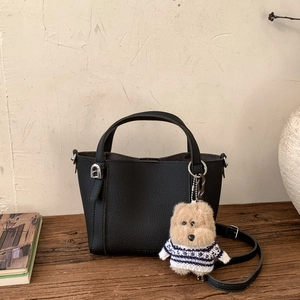 Detail view of black pebbled leather bucket bag with cute dog charm and detachable strap