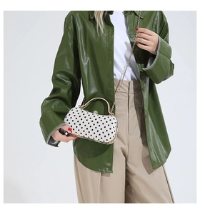 Detailed close-up of a white polka dot clutch with gold handle and crystal clasp on a model