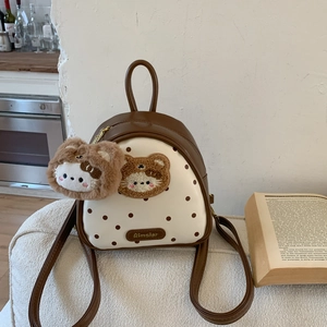 Detailed view of mini brown leather backpack with polka dot fabric and plush bear pendant