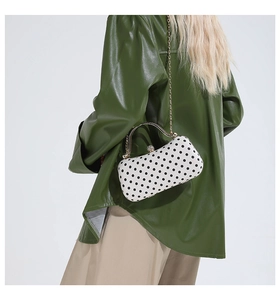 Detailed view of luxury polka dot hard shell clutch with gold chain strap on model