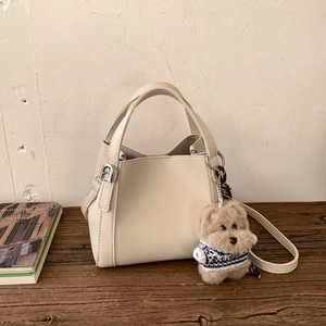 Detail of cream leather bucket bag with litchi texture and a cute plush dog pendant