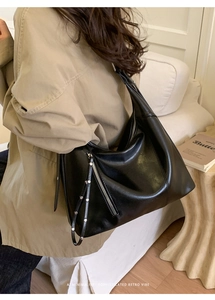 Detail of black glossy leather hobo bag with silver zipper and stud accents on model
