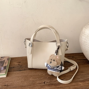 Detail of cream lychee leather bucket bag with cute brown plush puppy charm
