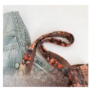 Detail of soft plush tote bag featuring orange and brown plaid texture with wide handle