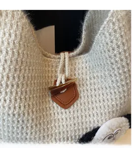 Detail of beige knit tote with brown leather horn buckle and plush cartoon elements