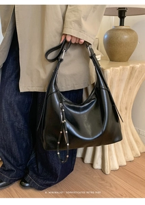 Detail of a minimalist black leather half-moon bag with silver studs and long puller