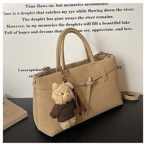 Detail of khaki suede tote bag with decorative buckle and plush bear charm accessory
