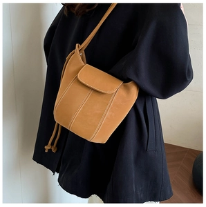 Detail of brown bucket bag with contrast stitching and drawstring on a model