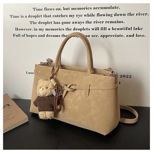 Detail of a beige tote bag featuring a teddy bear charm and narrow belt-style buckles