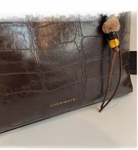 Detail of dark brown stone textured tote bag with golden logo and vintage bead charm
