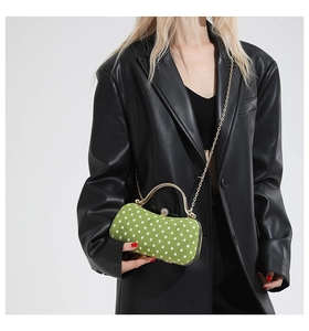 Close-up of green polka dot box bag with gold chain held against black leather jacket