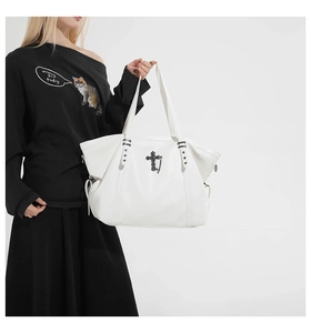 Detail of white leather tote bag featuring gothic black cross and star rivets