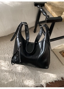 Detail of black glossy leather tote bag with silver zippers on a beige shaggy rug