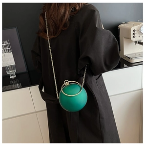 Close-up of a green spherical evening bag with golden metal ring handle and chain strap