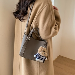 Detail of dark grey litchi grain bucket bag with a cute teddy bear plush charm
