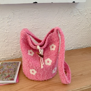 Detailed close-up of pink fluffy drawstring bucket bag with white floral pattern on a wood desk