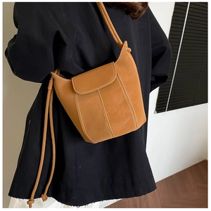 Close-up of camel leather bucket bag with white stitching on model's shoulder