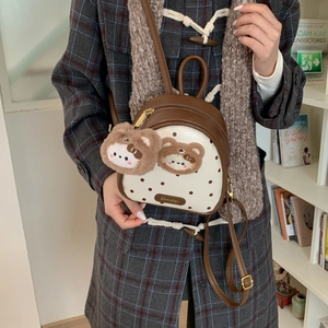Detail of mini backpack with brown accents, plush bear charm, and dotted pattern design