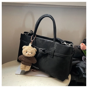 Macro detail of matte black tote bag with buckle strap and cute teddy bear pendant