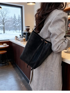 Détail du sac cabas en cuir noir mat avec cordon de serrage latéral porté à l'épaule