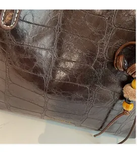 Detail of dark brown faux-croc tote with creative earphone charm and glossy finish