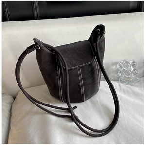 Close-up of black leather bucket bag with white contrast stitching and shoulder strap