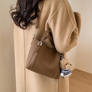 Detail of brown litchi pattern bucket bag with a cute bear charm and adjustable strap