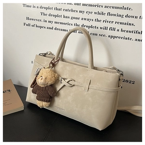 Detail of beige minimalist handbag with knot decor and a brown plush bear keychain