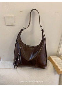 Detail of dark brown glossy crossbody bag with silver zipper and long fringe tassel