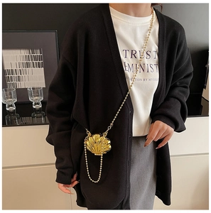 Detail of a golden shell-shaped mini bag with metallic texture and sleek ball chain