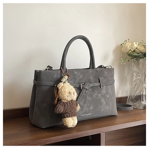 Detail view of a dark grey faux suede tote bag featuring a cute teddy bear charm