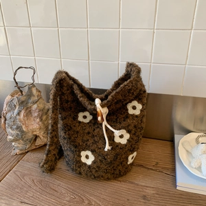 Detail of plush brown knit bucket bag with white floral pattern and drawstring closure
