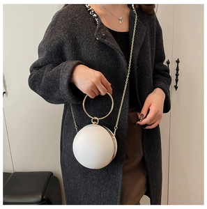 Macro detail of white spherical clutch bag with golden round handle and chain strap