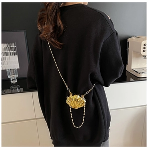 Detail of a golden shell-shaped mini crossbody bag with a fine ball chain on a black outfit