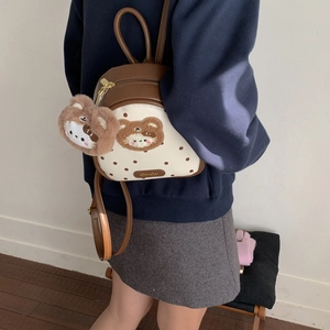 Detail of a brown polka dot backpack with a plush bear charm and metallic Aimeter logo