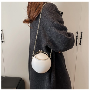 White spherical handbag with gold ring handle and chain strap on a grey sweater