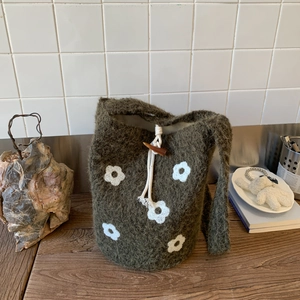 Close-up of dark green knitted bucket bag with white floral pattern and horn toggle closure