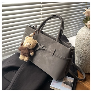 Detail of grey matte handbag featuring decorative knot straps and a brown bear pendant