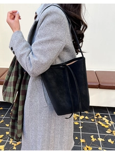 Sac seau minimaliste en cuir noir avec cordon porté dans une scène de rue automnale
