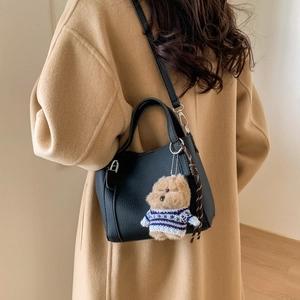 Detail of black textured leather bucket bag featuring a plush bear charm and strap