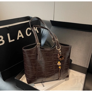 Close-up of dark brown crocodile texture tote bag with tassel charm and gold logo
