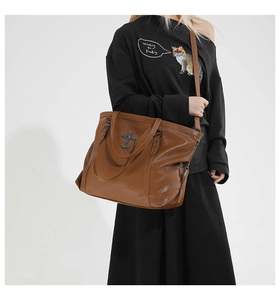Detailed view of brown leather tote bag with black metal cross and chain accessories