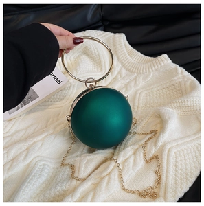 Detail of dark green spherical evening bag with golden circular handle and matte finish