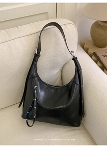 Detail of high-gloss black half-moon shoulder bag with silver hardware and studs on sofa
