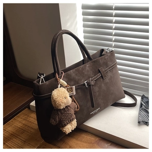 Detail of dark brown suede tote bag with decorative buckle and cute puppy plush charm