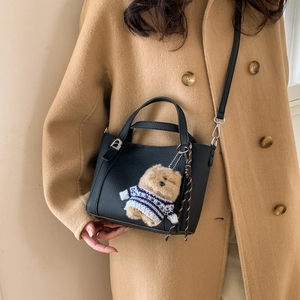 Detail of black pebbled leather bucket bag with cute bear charm worn with beige coat