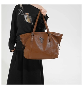Close-up of brown faux leather tote bag with metallic cross pendant and chain detail