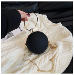 Detail of matte black spherical evening bag with golden ring handle and metal chain strap