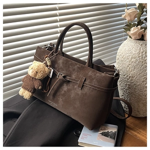 Detail of dark brown matte leather handbag with a plush bear charm in a lifestyle setting