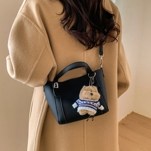 Detail of black pebbled leather bucket bag with cute bear charm on a camel wool coat